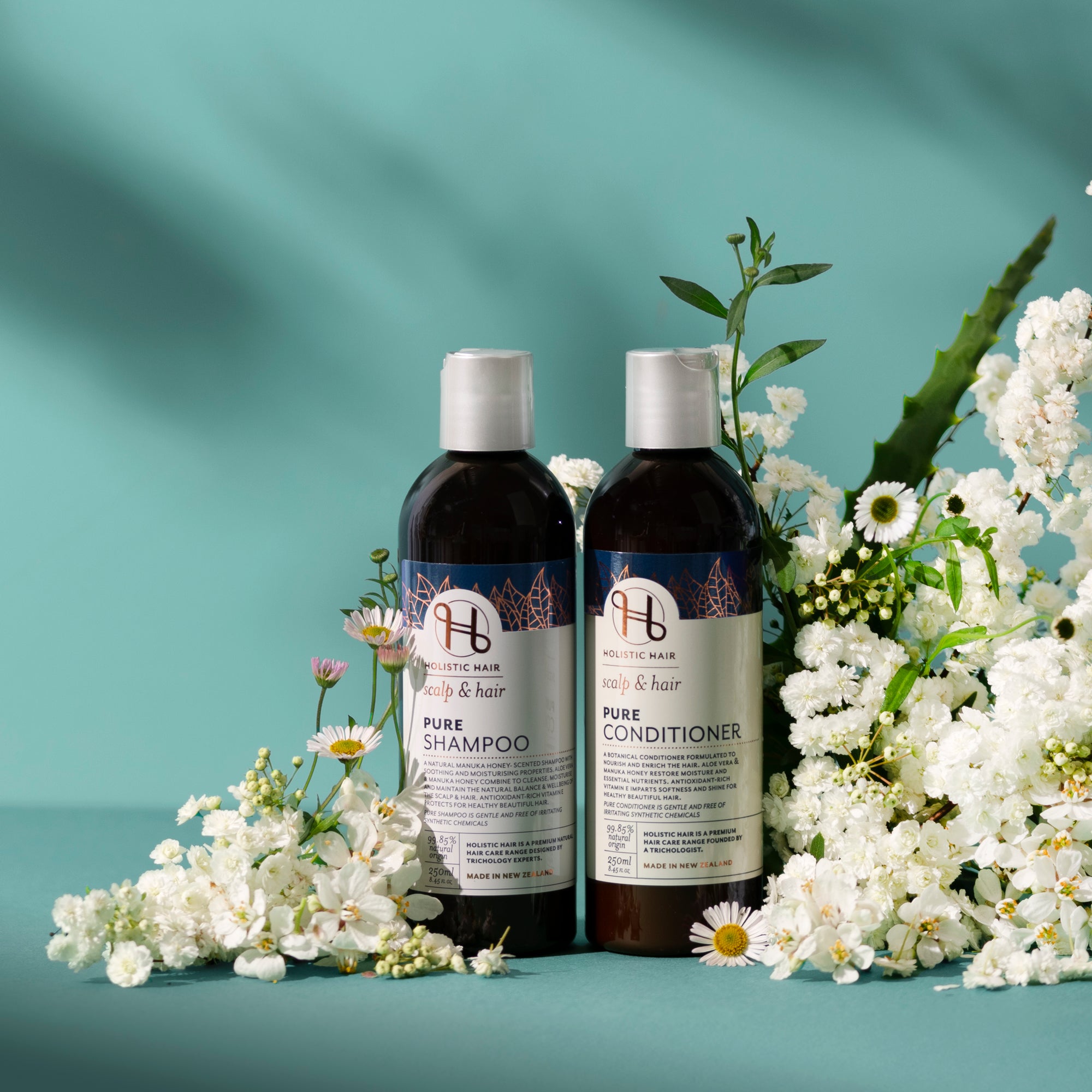 Two bottles of Pure shampoo and conditioner with flowers on a teal background